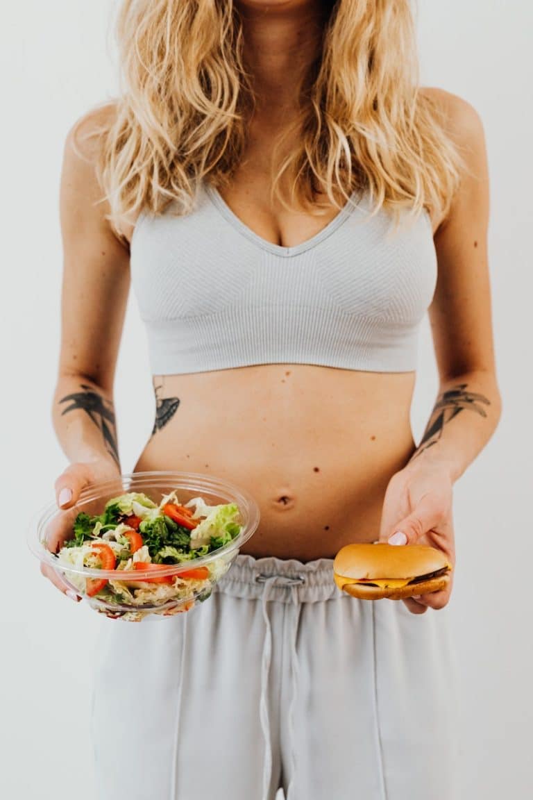Femme tenant un hamburger et un bol de salade